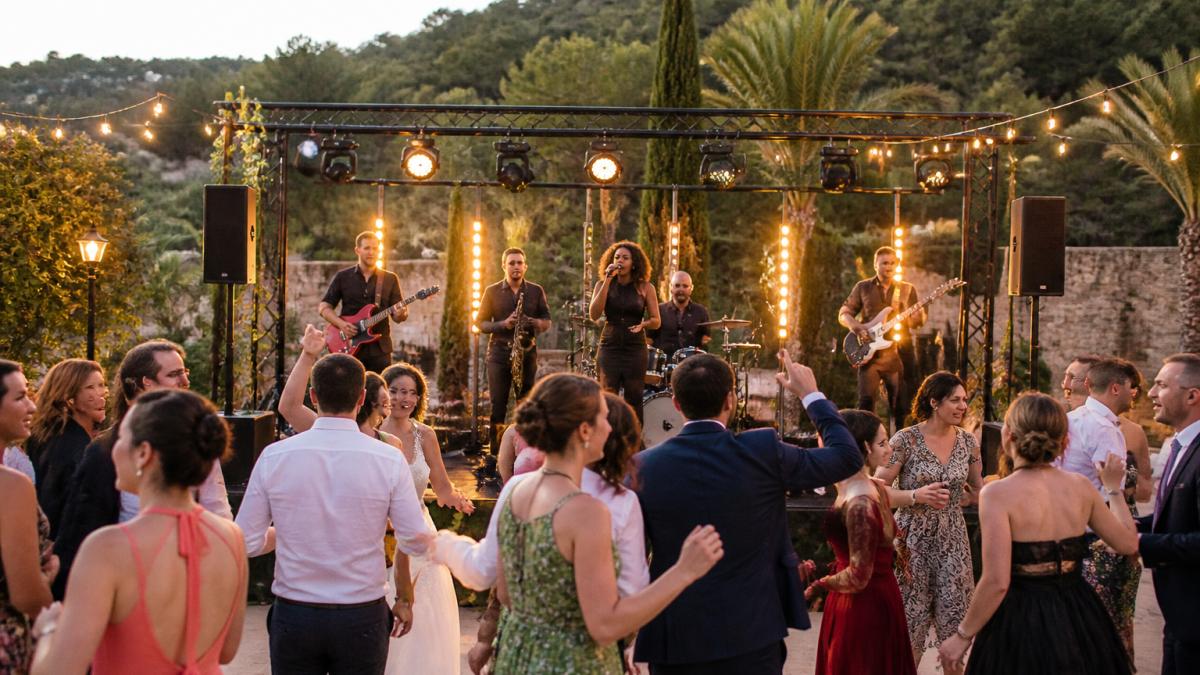 Grupo de música en directo como entretenimiento para bodas actuando ante invitados que bailan al aire libre.